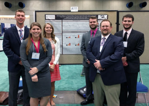 Pharmaceutical science pharmacy students pose in front of a research project